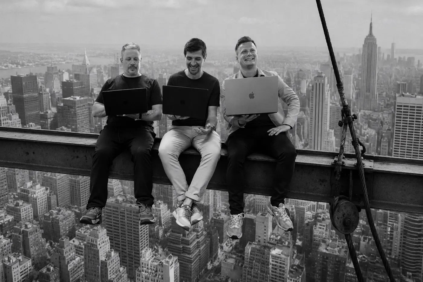 Stephan Kindler mit zwei Kollegen der OIT GmbH, alle mit Laptop auf einem Stahlträger vor der Skyline von New York